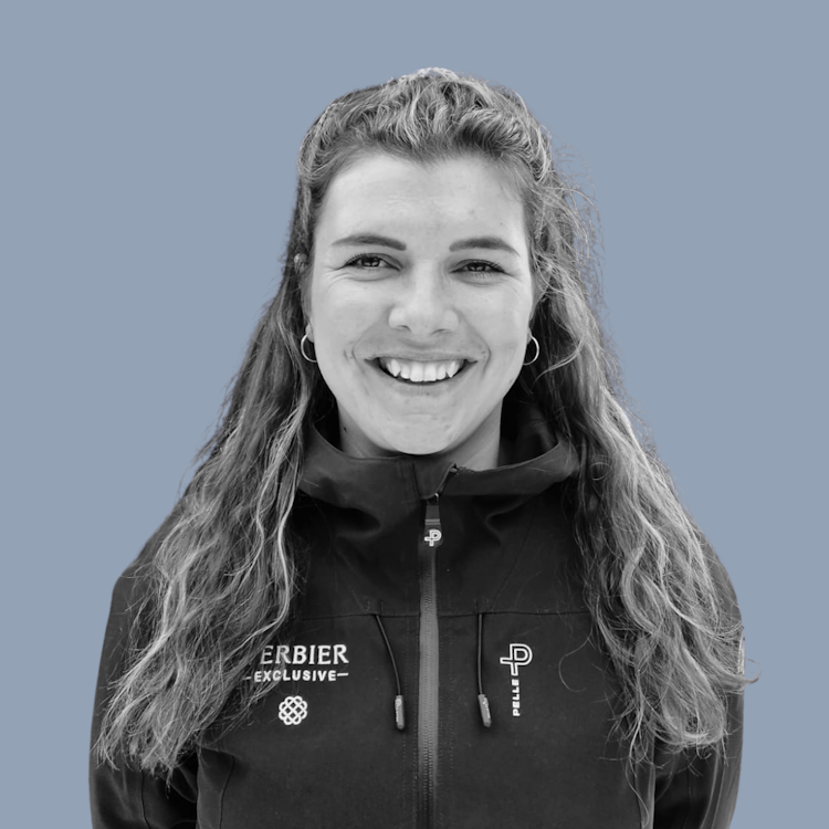A person wearing a puffer jacket stands smiling against a plain background.