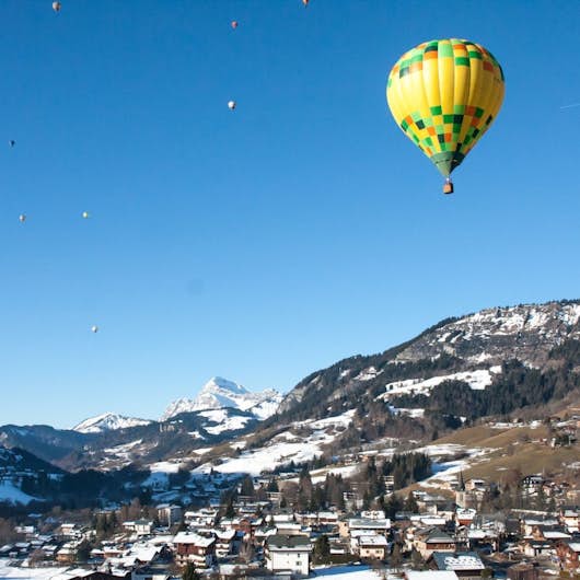 Person in a brown coat and white hat facing away, with snowflakes on their back, and hair blowing in the wind against a snowy backdrop