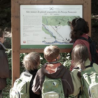 A family of four, wearing backpacks, reading an informational sign about a historical mining site in a forest.