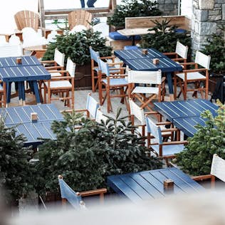Outdoor dining area with blue and white tables surrounded by potted evergreen trees, conveying a cozy, winter ambiance.