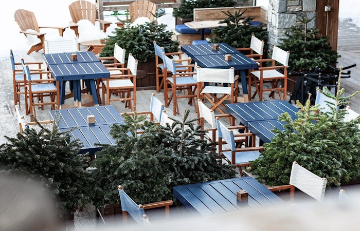 Blue and brown dining tables and chairs outside a restaurant surrounded by green plants 