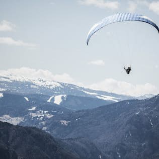 A paraglider soaring above snow-capped mountains under a clear sky.