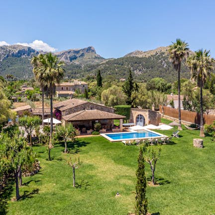 Aerial view of a luxurious estate with a large house, swimming pool, and manicured gardens surrounded by mountains.