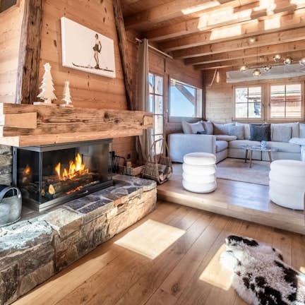La Cabane Cozy wooden cabin interior with a stone fireplace, plush seating, and soft lighting. Large windows illuminate the space with natural light.