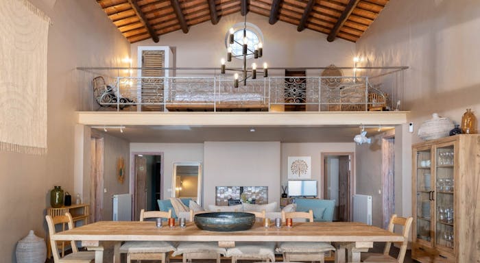 La Capella Interior Spacious rustic dining room with a wooden table, modern chandelier, and loft area. Exposed beams and soft lighting create a cozy ambiance.