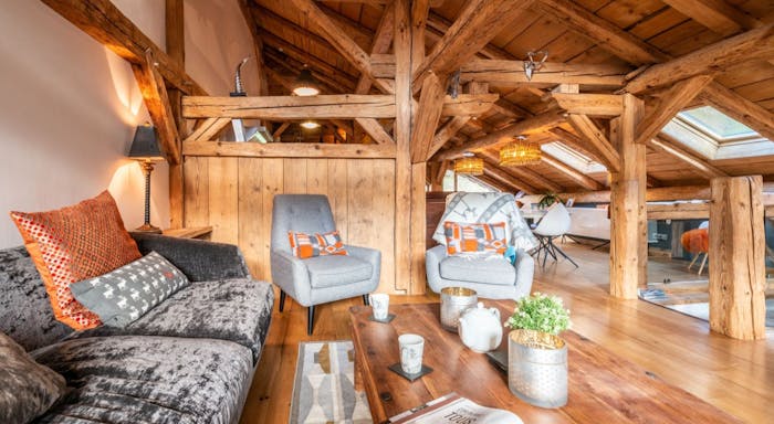 La ferme interior Cozy attic living space with wooden beams, a plush sofa, two armchairs, a coffee table, and a skylight illuminating the room.