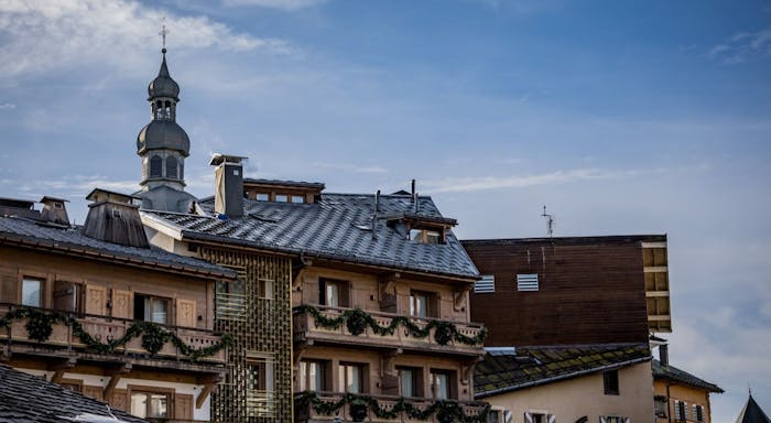 Snow-dusted rooftops of traditional buildings with a church spire in the background under a blue sky.