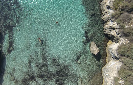 Aerial view of two people swimming in clear turquoise water near rocky shores.
