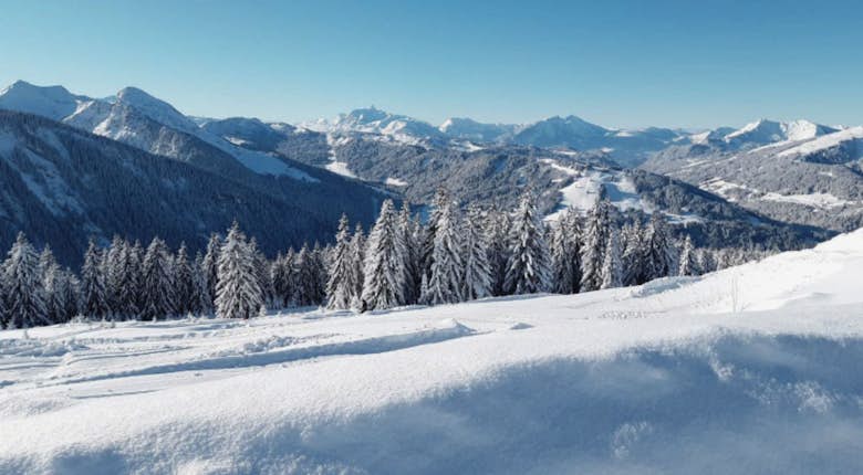 Snow-covered mountain peaks under a clear, dark blue sky. A faint trail is visible in the sky near the peaks.
