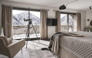 Champagny-en-Vanoise - 2 Champagny-en-Vanoise location - Chalet Sylora - Modern bedroom with a large bed, telescope by the window, and neutral-toned decor. It includes a wardrobe, TV, and seating area. Natural light streams through glass doors.