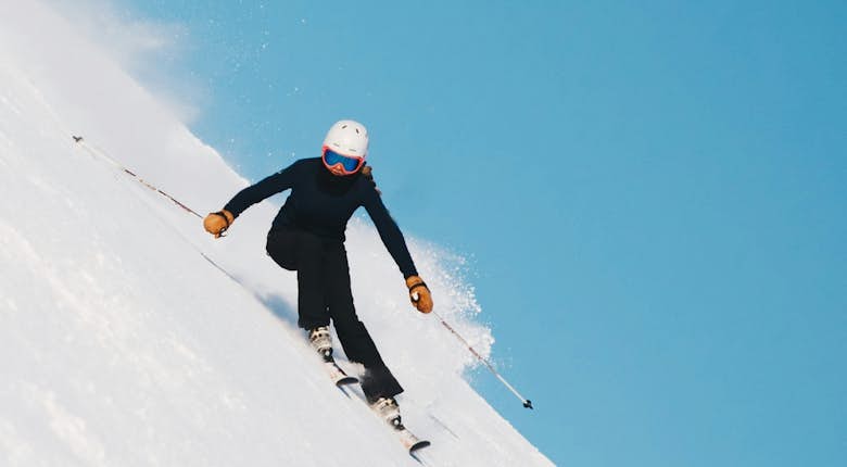Skier in blue suit and white helmet swiftly descending a snow-covered slope under a clear blue sky.