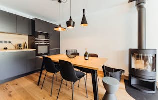 Megeve accommodation - Apartment Opale - Modern kitchen with a wooden dining table, black chairs, a fireplace, and pendant lights.