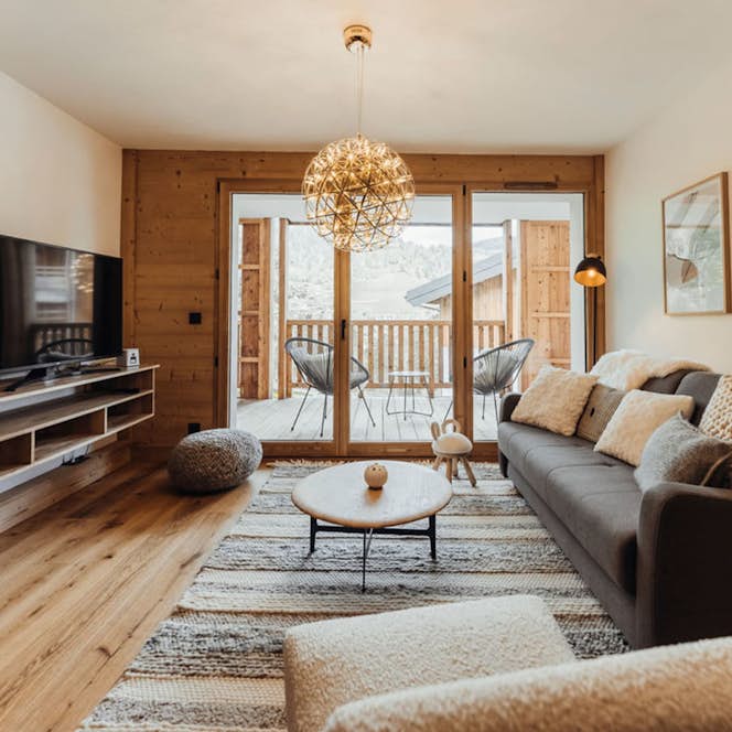 Megeve accommodation - Apartment Opale - A cozy living room with a modern sofa, wooden flooring, a television, and large doors opening to a balcony with a scenic outdoor view.