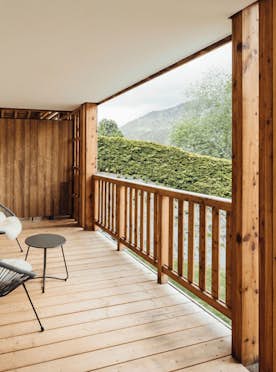 Megeve accommodation - Apartment Opale - A cozy wooden terrace with a modern chair and table, overlooking green hills, framed by open sliding doors.
