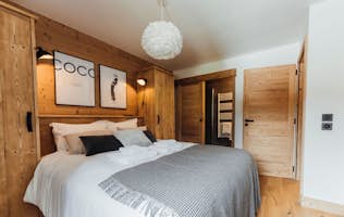 Megeve accommodation - Apartment Opale - A cozy bedroom with a white bed, gray blanket, wood panel walls, modern artwork, and a fluffy ceiling light.
