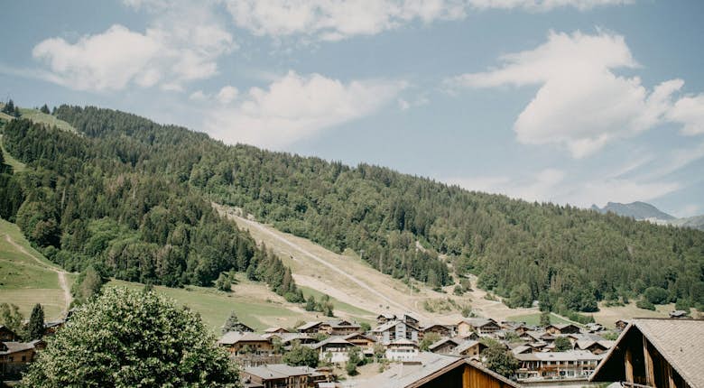 Scenic view of a mountain village with traditional houses nestled among lush green hills under a clear sky.