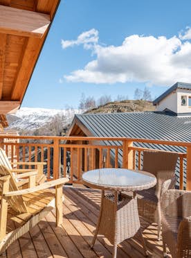Alpe d'Huez - 5 Alpe d’Huez accommodation - Apartment Ascar - A wooden balcony with outdoor seating, including a round table and chairs, overlooking rooftops under a clear sky.