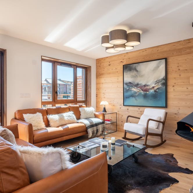 Alpe d'Huez - 1 Baqueira Beret alojamiento - Apartamento Écrin - Modern living room with tan leather sofas, a mounted abstract painting, cowhide rug, light wood panel wall, large windows, and a black suspended fireplace.