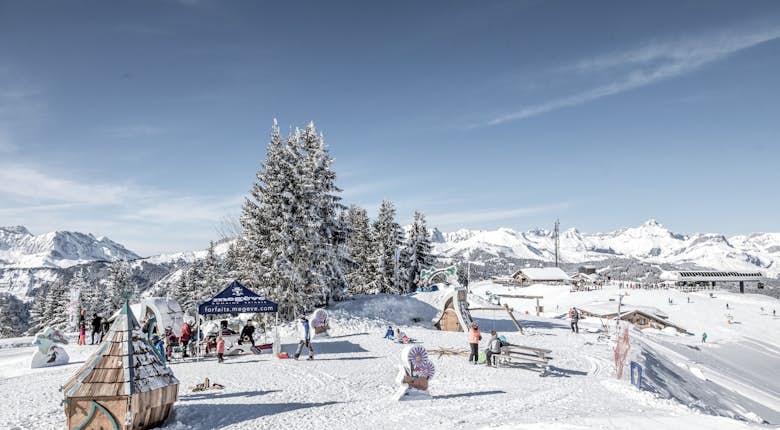 Snow-covered ski resort with people skiing and snowboarding. Mountains and trees in the background. Bright, clear sky.