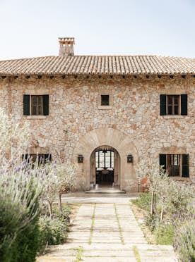 Mallorca accommodation - Can Tramuntana - A traditional stone house with a tiled roof and a pathway leading to the entrance, surrounded by a garden with lavender.