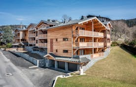 Les Gets alojamiento - Apartamento Colibri - Aerial view of a modern mountain residential area with wood-paneled buildings and a paved road in a european village.