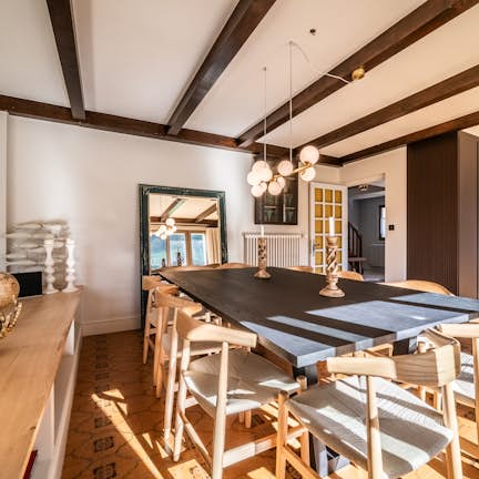 Interior of a modern home featuring a curved kitchen bar with a black stovepipe, wooden beams on the ceiling, and an adjoining dining area lit by natural light.