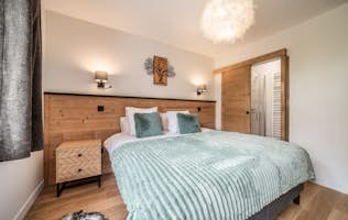 Alpe d'Huez - 3 Alpe d’Huez accommodation - Apartment Epicea - Modern bedroom featuring a large bed with white bedding and gold pillows, wooden accents, a mirrored closet, and minimalistic hanging light.