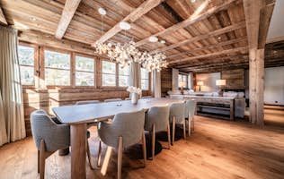 Les Gets  - 3 Les Gets accommodation - Chalet Savanna - Rustic dining room with wooden beams and walls, a large table with eight gray chairs, chandelier, and natural light from windows with beige curtains.