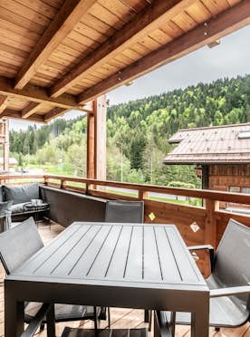 Les Gets - 5 Chamonix alojamiento - Apartamento Dolmen - Outdoor deck or terrace with wooden roof, modern black table and chairs, and cushioned seating area. Overlooks wooded hillside and rustic buildings.