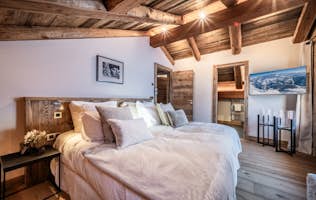 Saint-Gervais - 2 Meribel alojamiento - Chalet Betula - A cozy, rustic bedroom with wooden walls and ceiling, featuring a large bed, pillows, a window with a snowy view, and a landscape painting on the wall.
