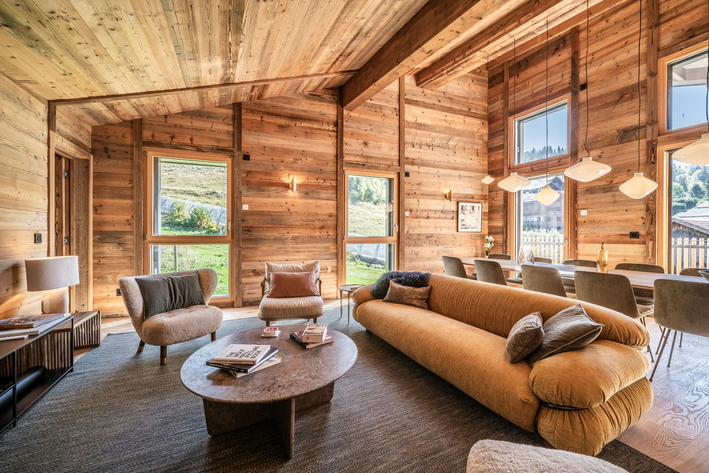 Apartment Tourmalet A wooden chalet in a snowy landscape with a hot tub on the patio. Surrounded by trees and mountains under a partly cloudy sky.