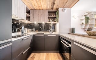 Les Gets accommodation - Apartment Colibri - Modern kitchen interior with sleek black cabinets, wooden accents, and built-in appliances, featuring a spacious countertop and stylish shelving.