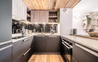 Les Gets - 3 Les Gets location - Appartement Colibri - Modern kitchen interior with sleek black cabinets, wooden accents, and built-in appliances, featuring a spacious countertop and stylish shelving.