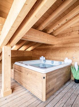 Châtel - 5 Châtel location - Appartement Nightfall - A wooden attic room with a hot tub, small potted plant, black bench, and a sliding glass door opening to a balcony.