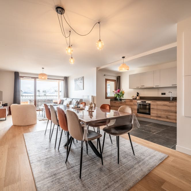Alpe d'Huez - 1 Alpe d’Huez accommodation - Apartment Epicea - Modern kitchen interior with wooden cabinets and countertops, stainless steel appliances, and a long dining table, all with a view of mountains through large windows.