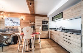 Châtel location - Appartement Chamoisine - Modern kitchen with light wood cabinetry, built-in appliances, and a dining area featuring a wooden table, chairs, and a bench. A wall photo of a skier adds a decorative touch. Châtel location - Appartement Chamoisine - Modern kitchen with light wood cabinetry, built-in appliances, and a dining area featuring a wooden table, chairs, and a bench. A wall photo of a skier adds a decorative touch.