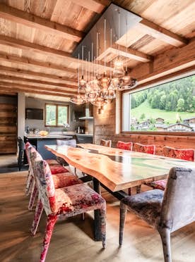 Morzine - 5 Morzine location - Chalet Kerasia - A modern dining room with a wooden table, mixed-patterned chairs, abstract paintings on the wall, and a contemporary light fixture. The room has wooden flooring and exposed ceiling beams.