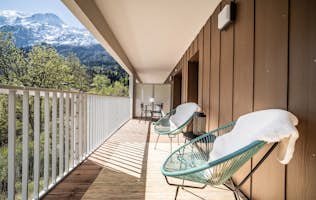 Les Houches - 4 Chamonix accommodation - Apartment Omas - A spacious balcony with two chairs and a small table overlooks trees and mountains under a clear blue sky.