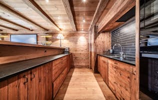 Verbier - 4 Verbier accommodation - Apartment Snowcrest - Wooden kitchen interior with exposed beams, wooden cabinets, and a black countertop. The space includes a backsplash and built-in appliances. Warm lighting enhances the rustic design.