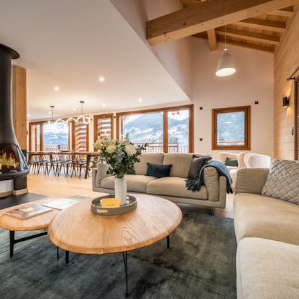 Cozy living room with a modern fireplace, plush sofas, wooden beams, and large windows showing mountain views.