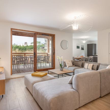 Apartment Oravo, Praz-sur-Arly Modern living room with a gray sectional sofa, wooden TV stand, wall-mounted TV, and sliding doors leading to a balcony with outdoor seating.