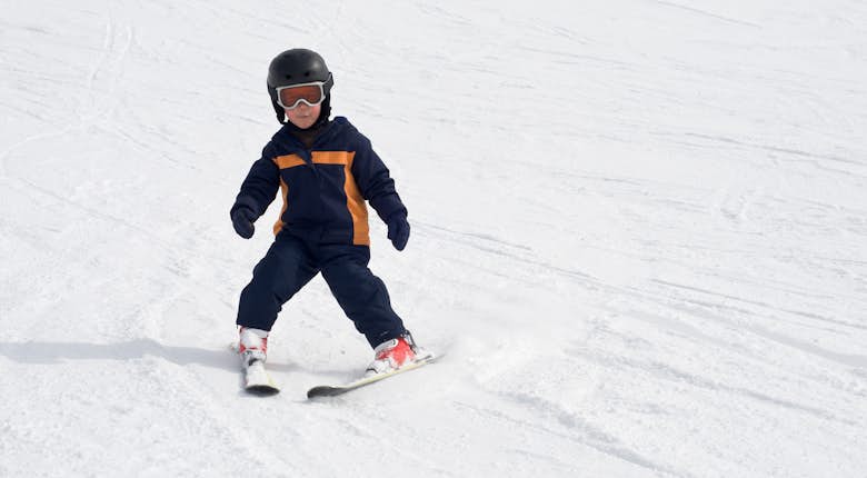 Young skier in helmet and goggles smoothly skiing down a snowy slope.