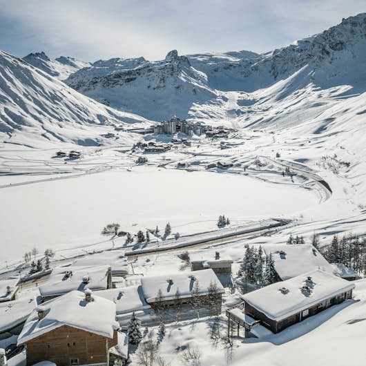 Snow-covered alpine village nestled in a valley with sunlit mountains in the background.