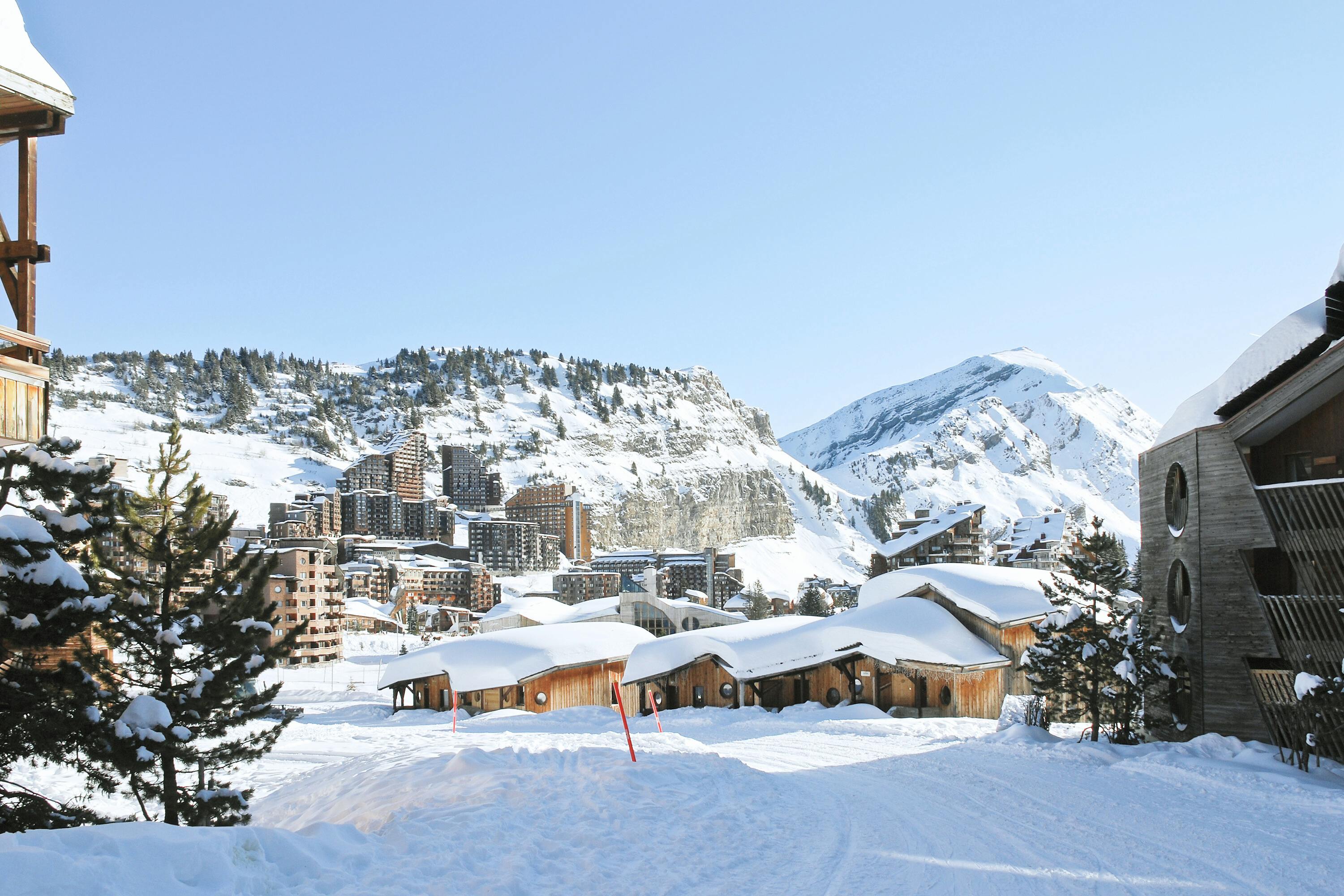 French Ski Resorts Near Geneva | Emerald Stay Alpine ski resort with snow-covered buildings and mountains in the background under a clear blue sky.