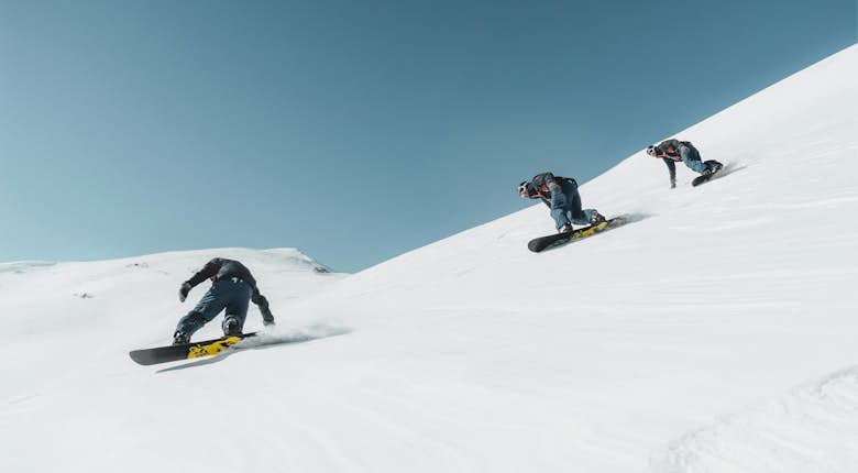 Three people snowboarding down a snowy mountain slope under a clear blue sky.