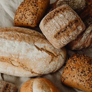Boulangerie le Montagnard Various loaves and rolls of artisan bread, some topped with seeds, arranged on a light cloth surface.