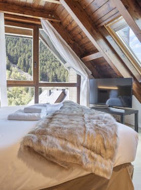 Val de Ruda - 5 Baqueira Beret location - Appartement Galena - A cozy attic bedroom with slanted wooden ceilings, twin beds with green linens, a wooden nightstand, two windows, and a clear view of a mountain through a skylight.
