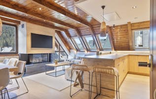 Val de Ruda - 2 Baqueira Beret location - Appartement Galena - A modern kitchen and dining area with wooden furniture, a table set for four, pendant lights, and large windows allowing natural light. The room features light wood flooring and beige tones.
