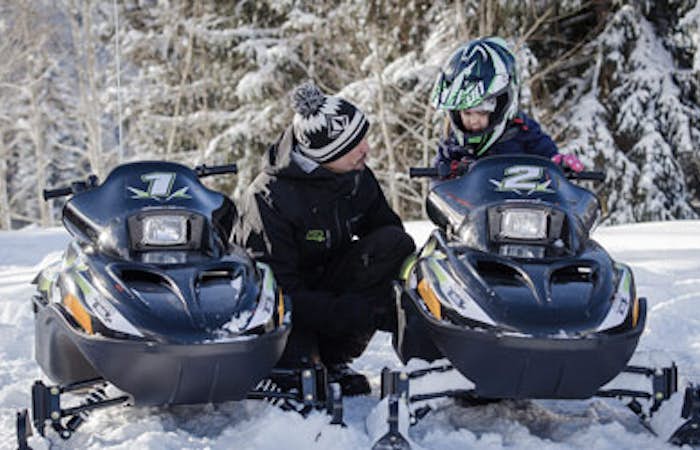 A father guiding his son on the electric snowmobile activity in Les Arcs