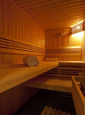 Verbier - 5 Verbier alojamiento - Atico Treize Etoiles - A wooden sauna interior with benches, a rolled white towel, a heater with stones, and warm ambient lighting.